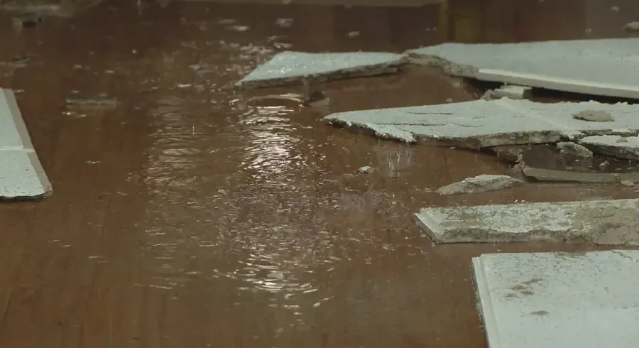 Water across a wood floor below fallen ceiling panels after an overhead pipe leak