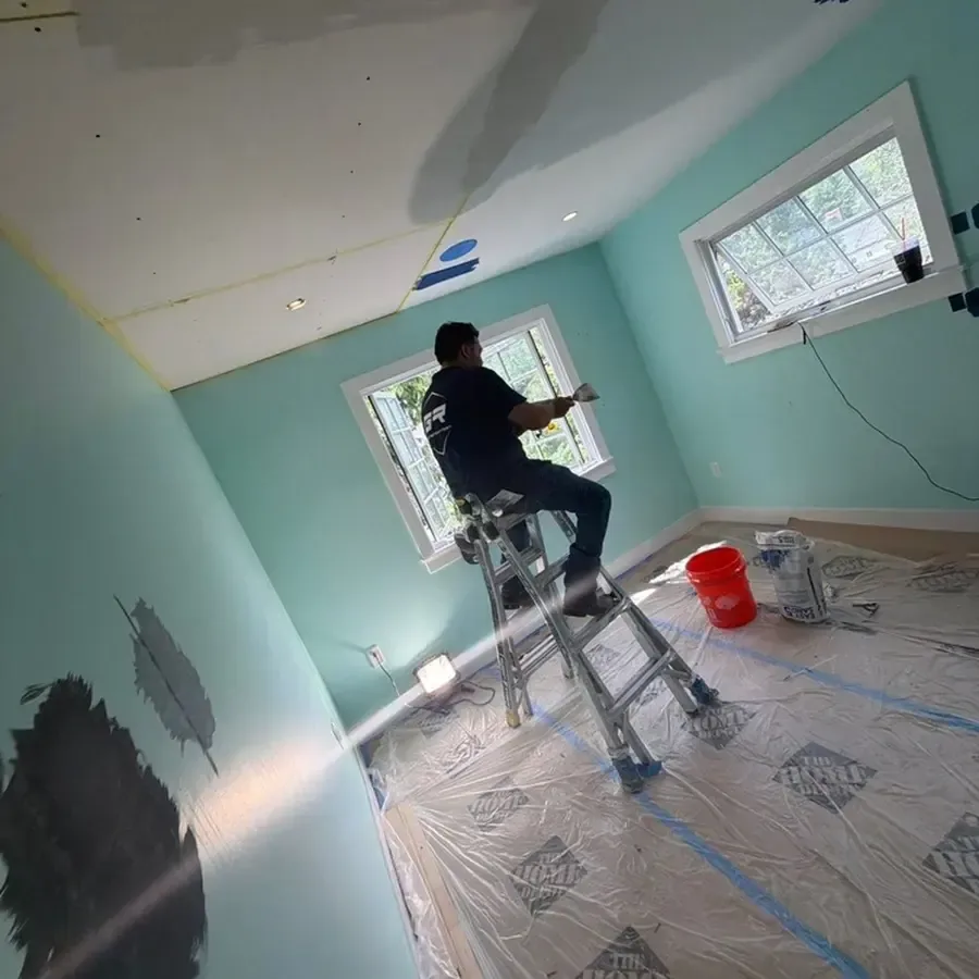 A worker on a ladder above protective floor sheeting