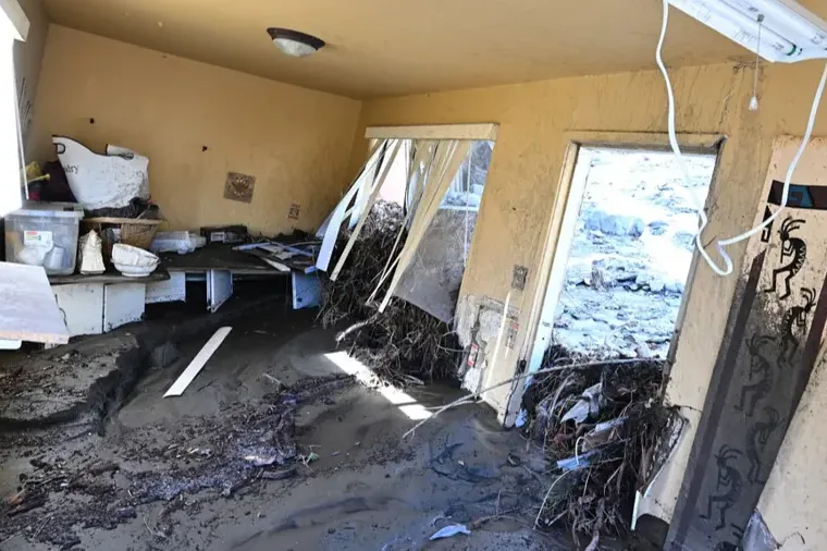 Mud and debris inside a home behind damaged exterior doors